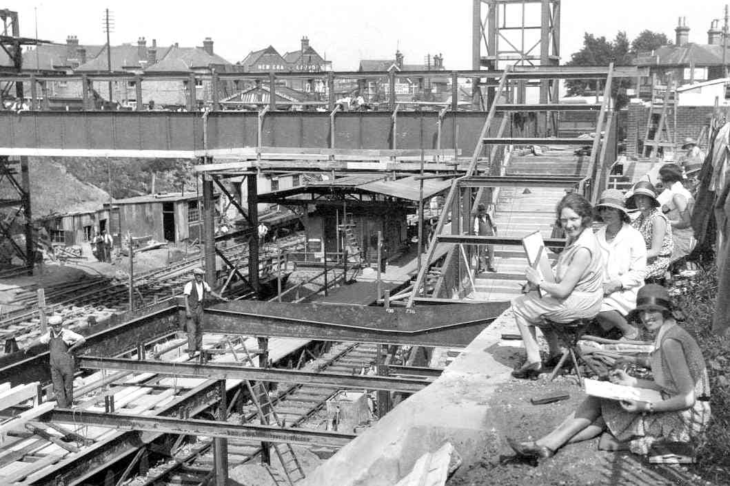 Black and white photograph of construction work at Pokesdown Station in about 1930. There are two workmen on the left, and on the right is a row of women sat drawing the scene.