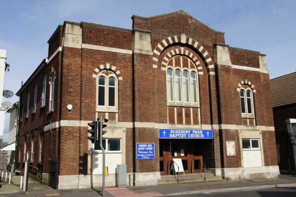 colour photo of square red brick building and blue sign with white writing saying Rosebery Park Baptist Church
