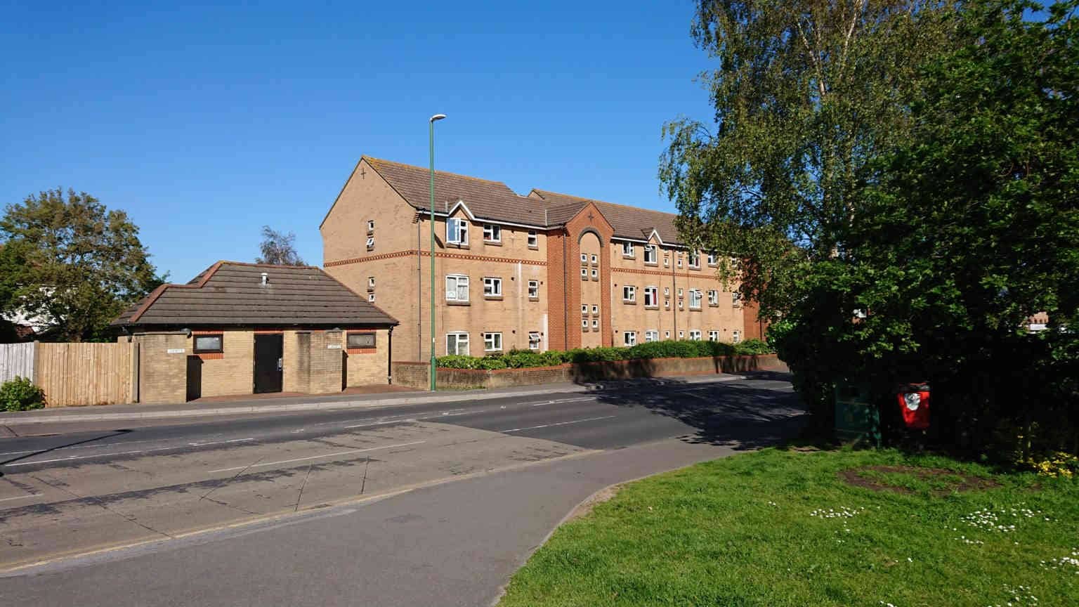 A colour photo of a block of public toilets and a three storey block of beige brick flats.
